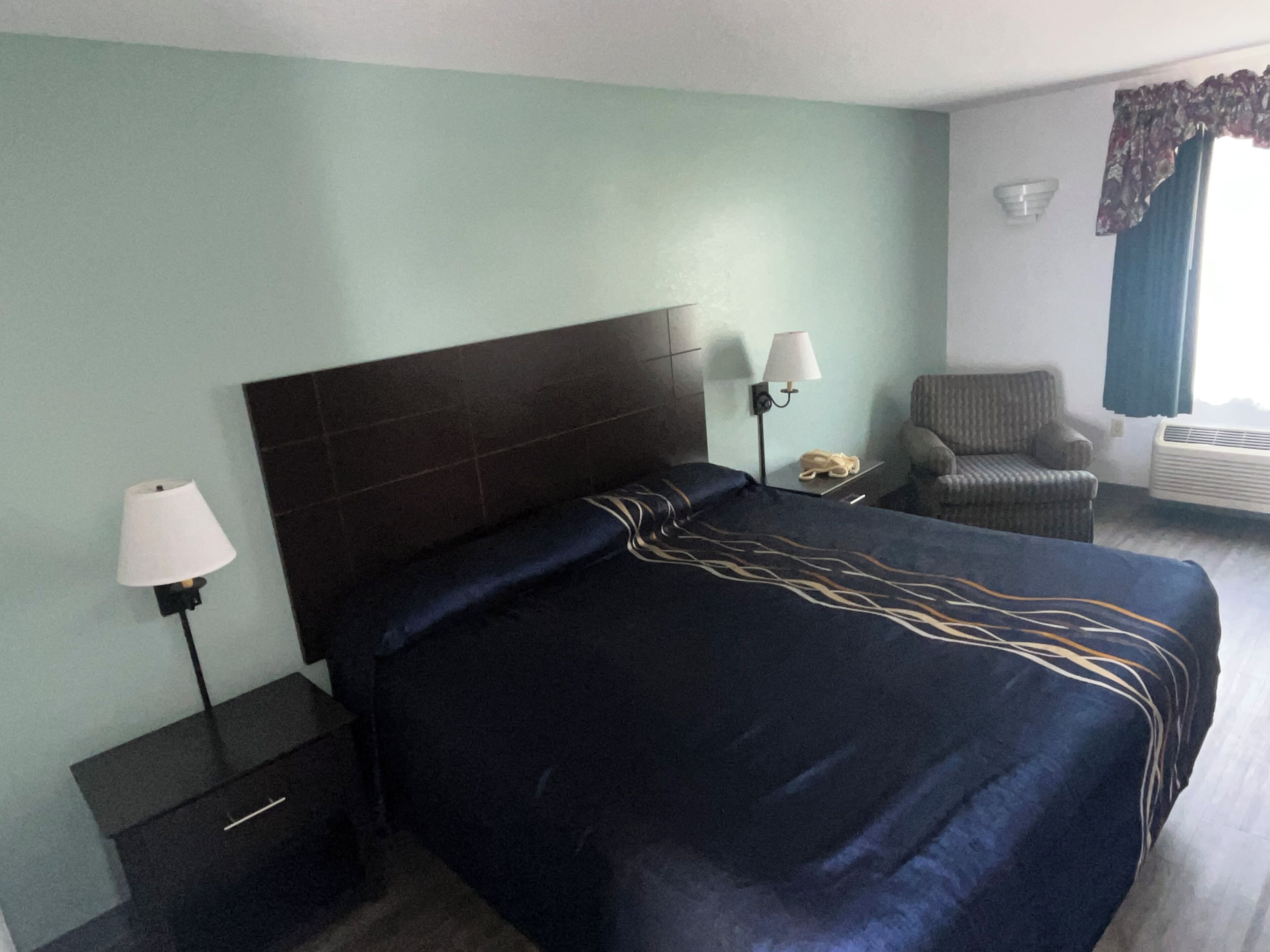 Ein Hotelzimmer mit einem großen Bett, einem Sessel, einem Nachttisch, einer Lampe und einem Telefon.
