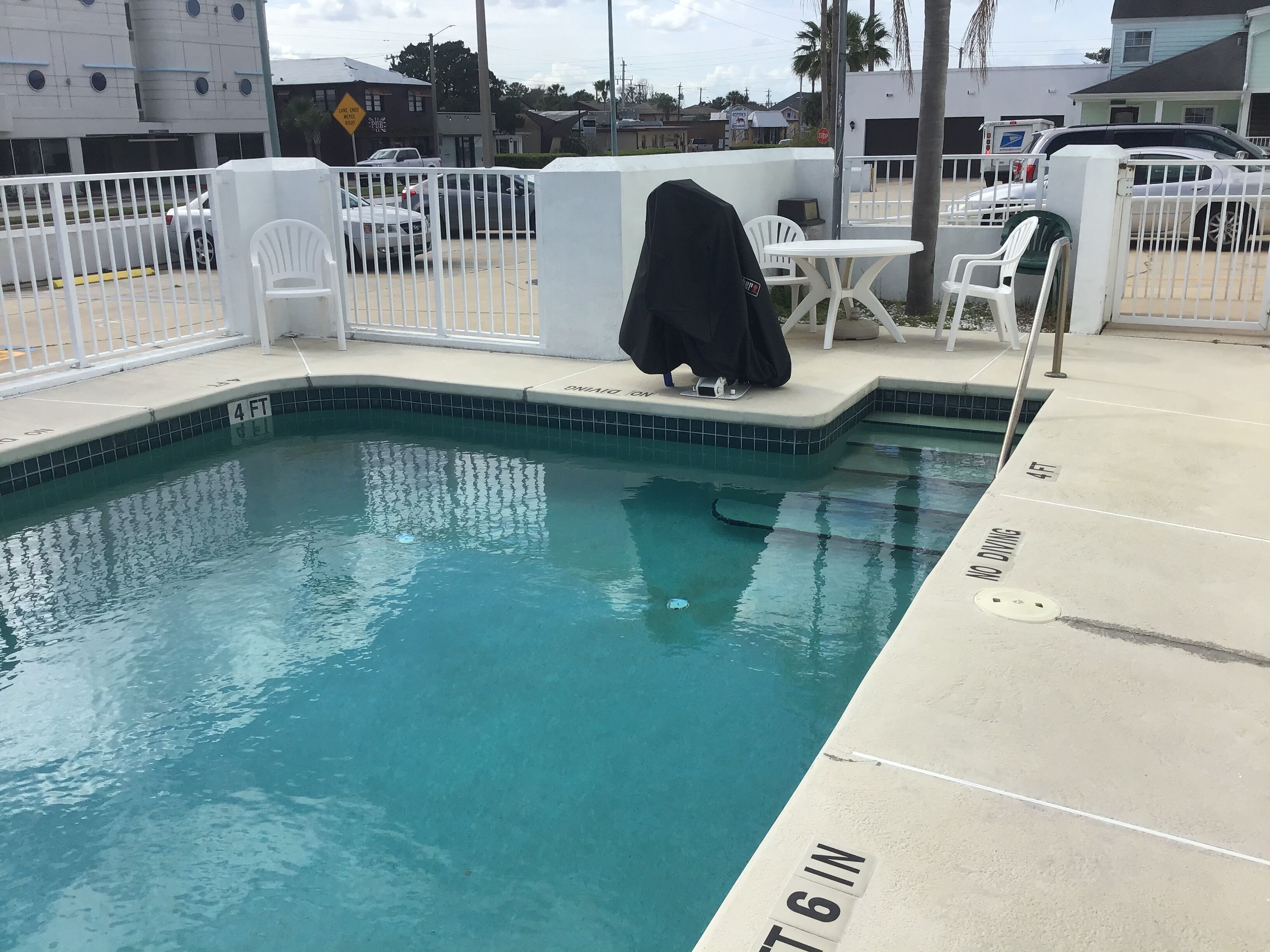Une piscine dont la profondeur est indiquée à 4 pieds, un espace abrité avec des chaises, et une autre indication de profondeur à 6 pouces.