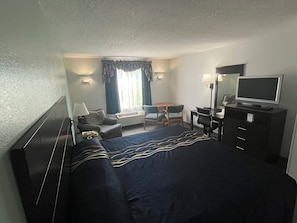 A hotel room with a bed, a desk, a chair, a television, and a window with curtains. - The Anastasia Inn (St. Augustine)