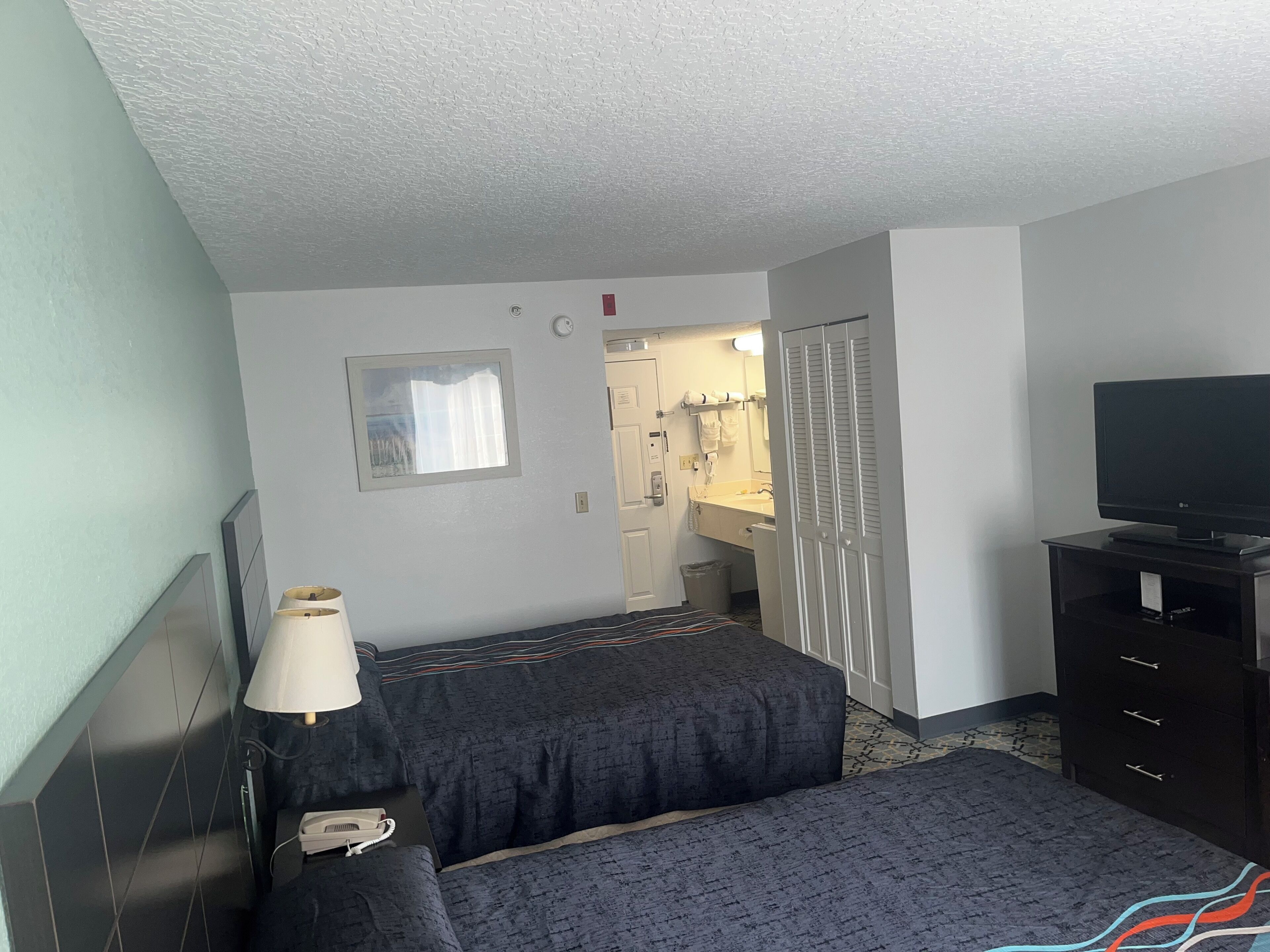 A hotel room with a bed, bedside table, lamp, TV, and a bathroom visible through an open door.