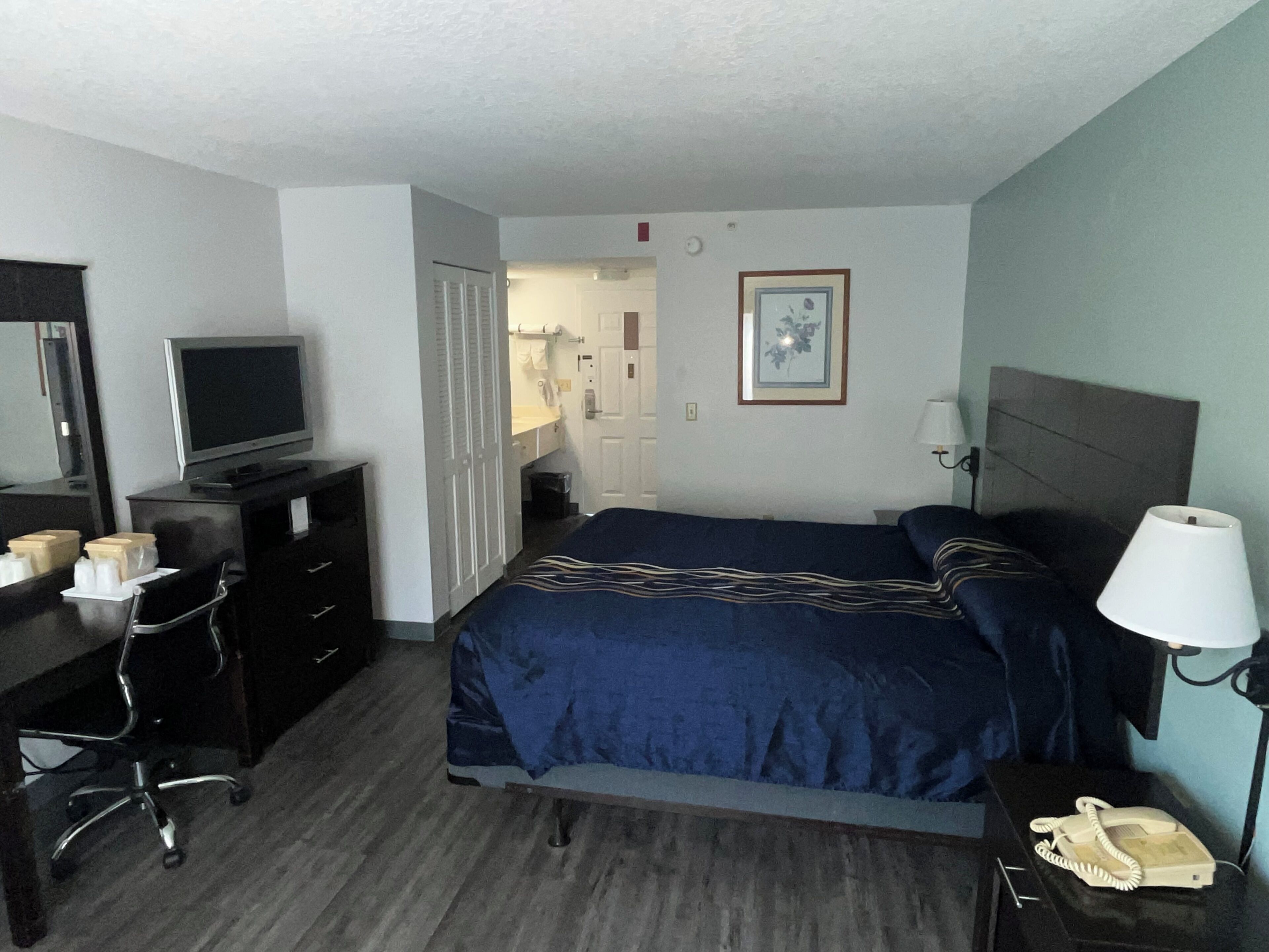 A hotel room with a bed, a desk with a computer, a telephone, and a television.