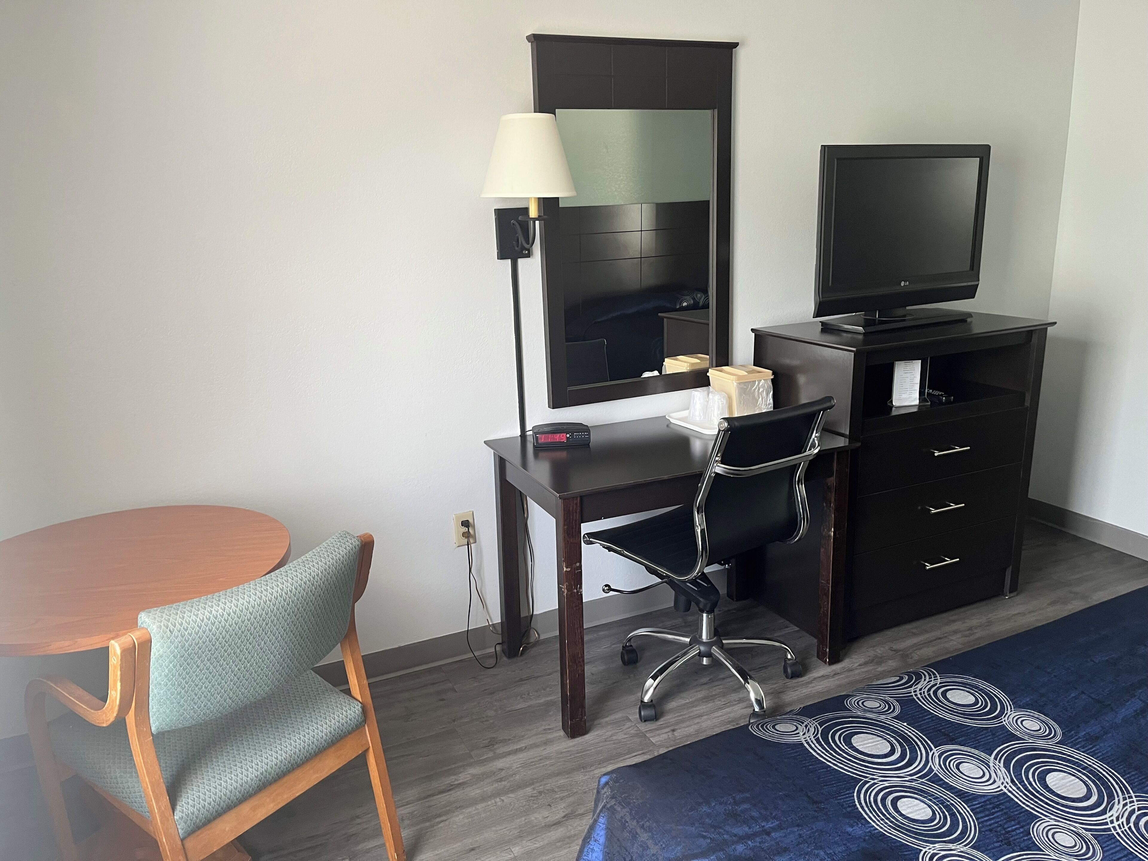 A hotel room with a desk, chair, television, and a bed with a patterned bedspread.