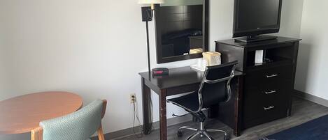 A hotel room with a desk, chair, television, and a bed with a patterned bedspread.