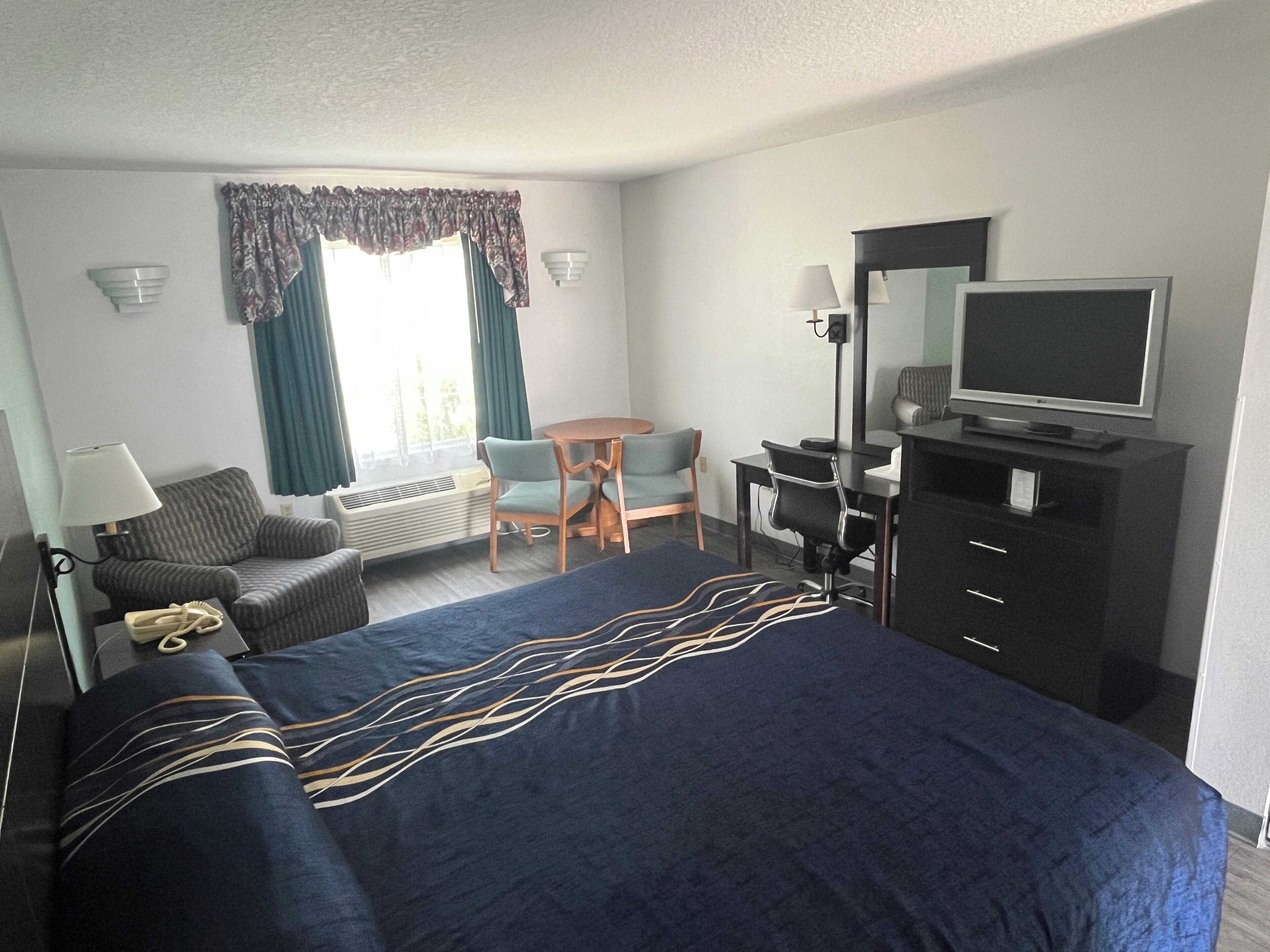 A hotel room with a bed, desk, chair, television, and a window with curtains.