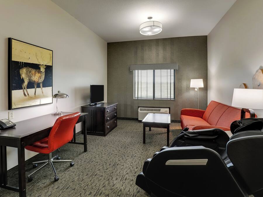 Une chambre d’hôtel équipée d’un bureau, d’un fauteuil de bureau rouge, d’un canapé en cuir noir et d’un grand tableau représentant un cerf.