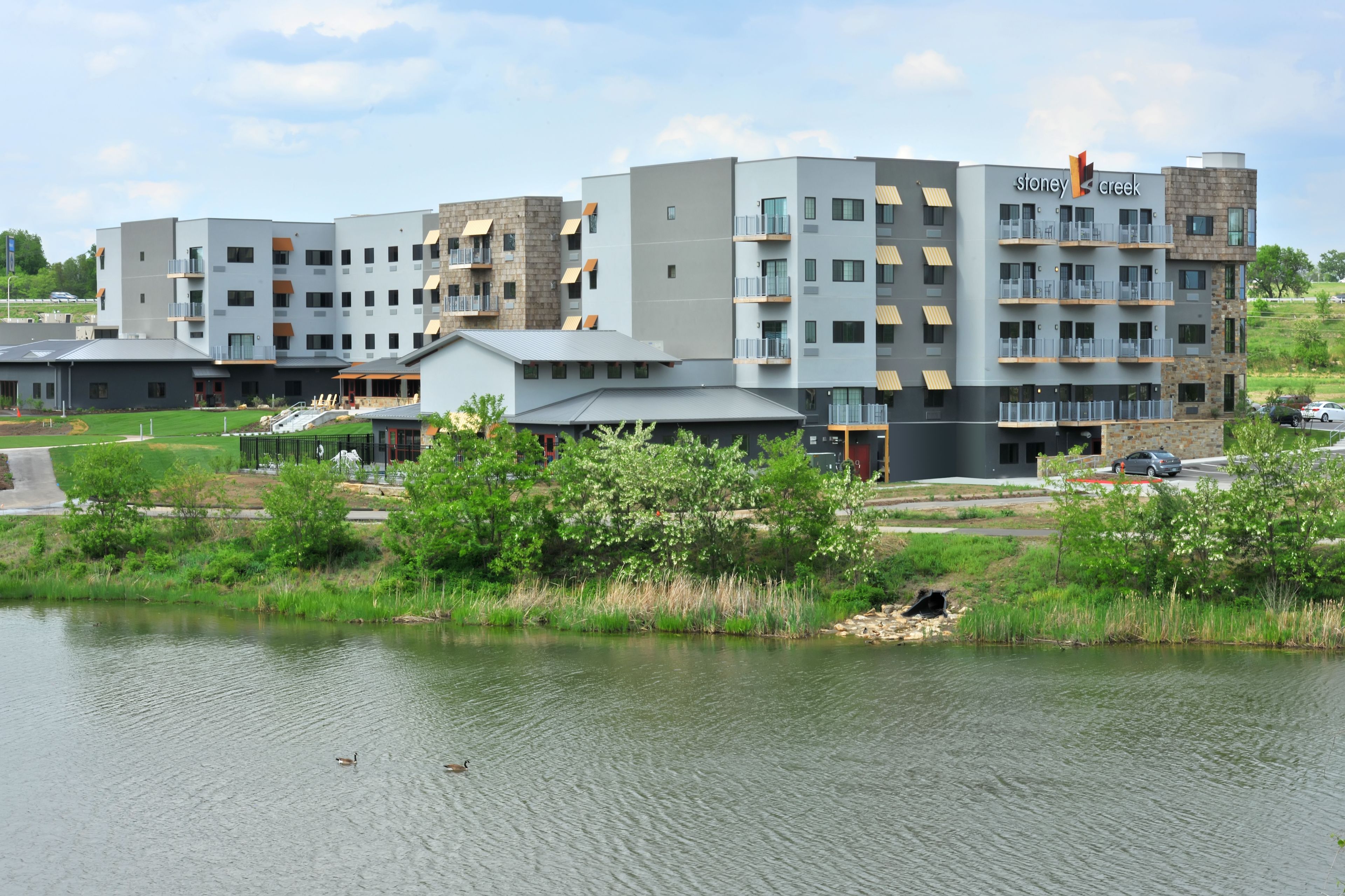 A modern hotel with multiple floors, balconies, and a view of a lake.