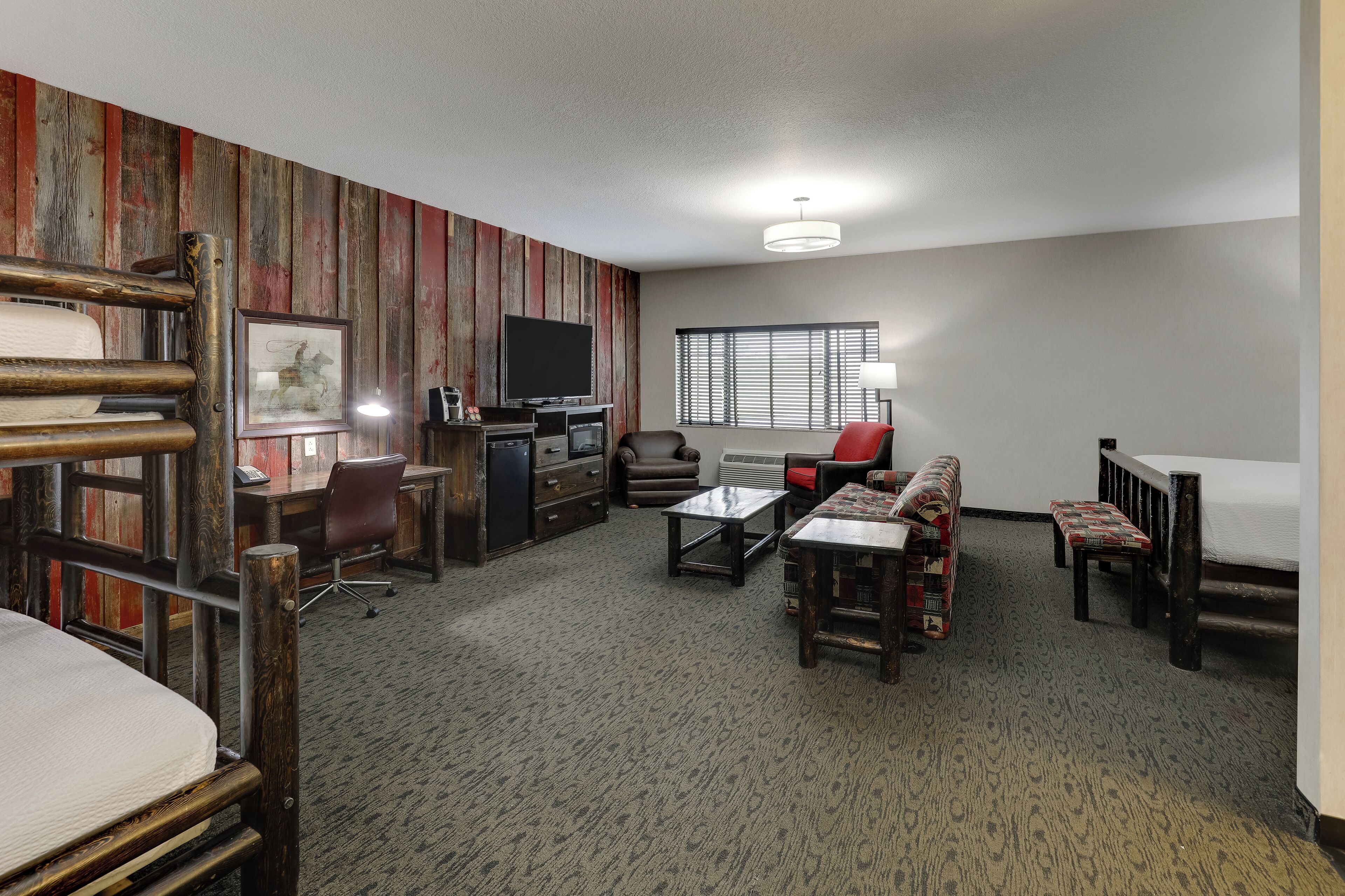 Una habitación de hotel con una cama litera, un escritorio con computadora, un televisor, un sofá y una ventana con persianas.