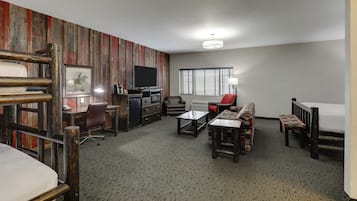 A hotel room with a bunk bed, a desk with a computer, a TV, a sofa, and a window with blinds.