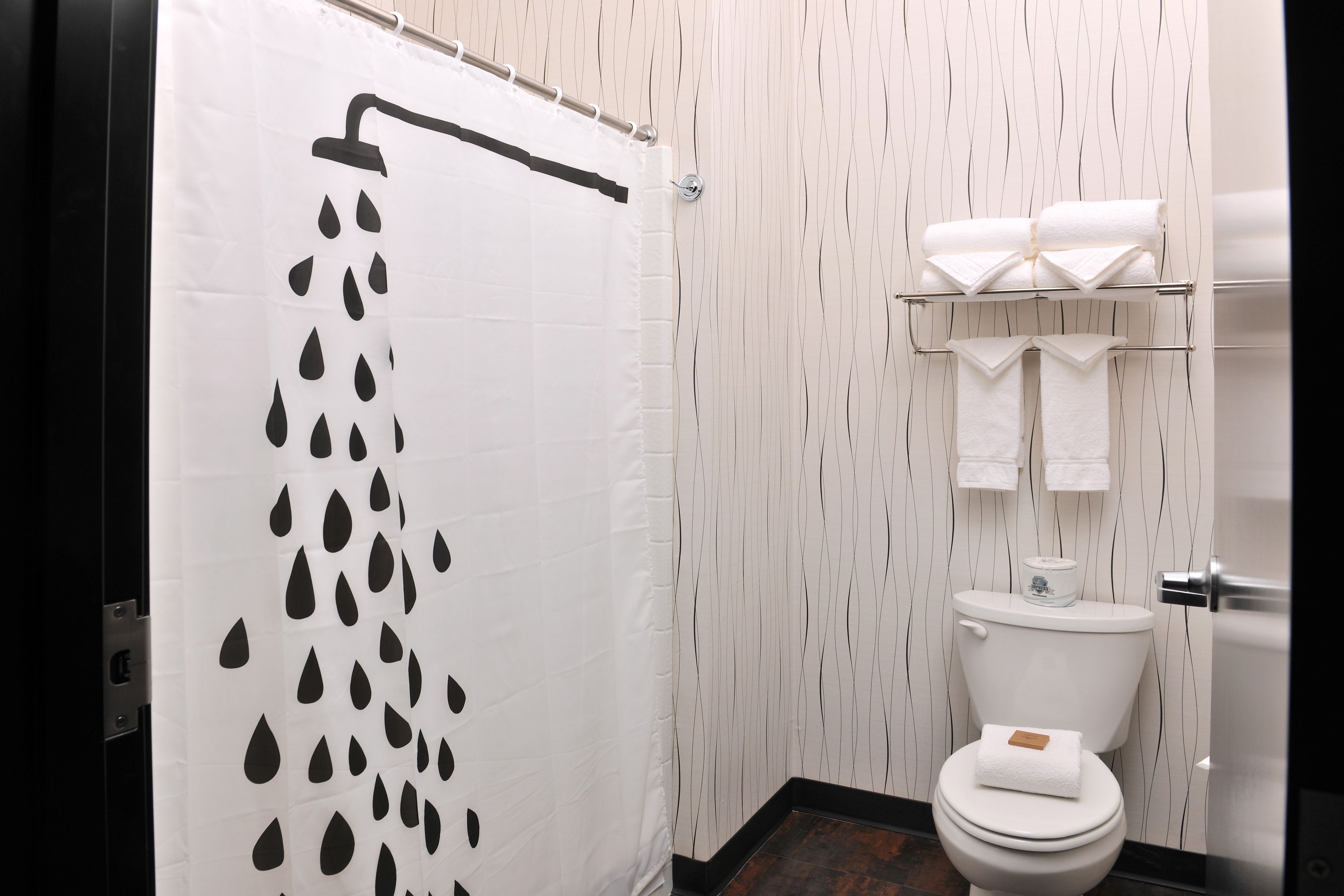 Ein Badezimmer mit Duschvorhang mit Regenmuster, Toilette mit einem Handtuch darauf und Handtuchhalter mit Handtüchern.