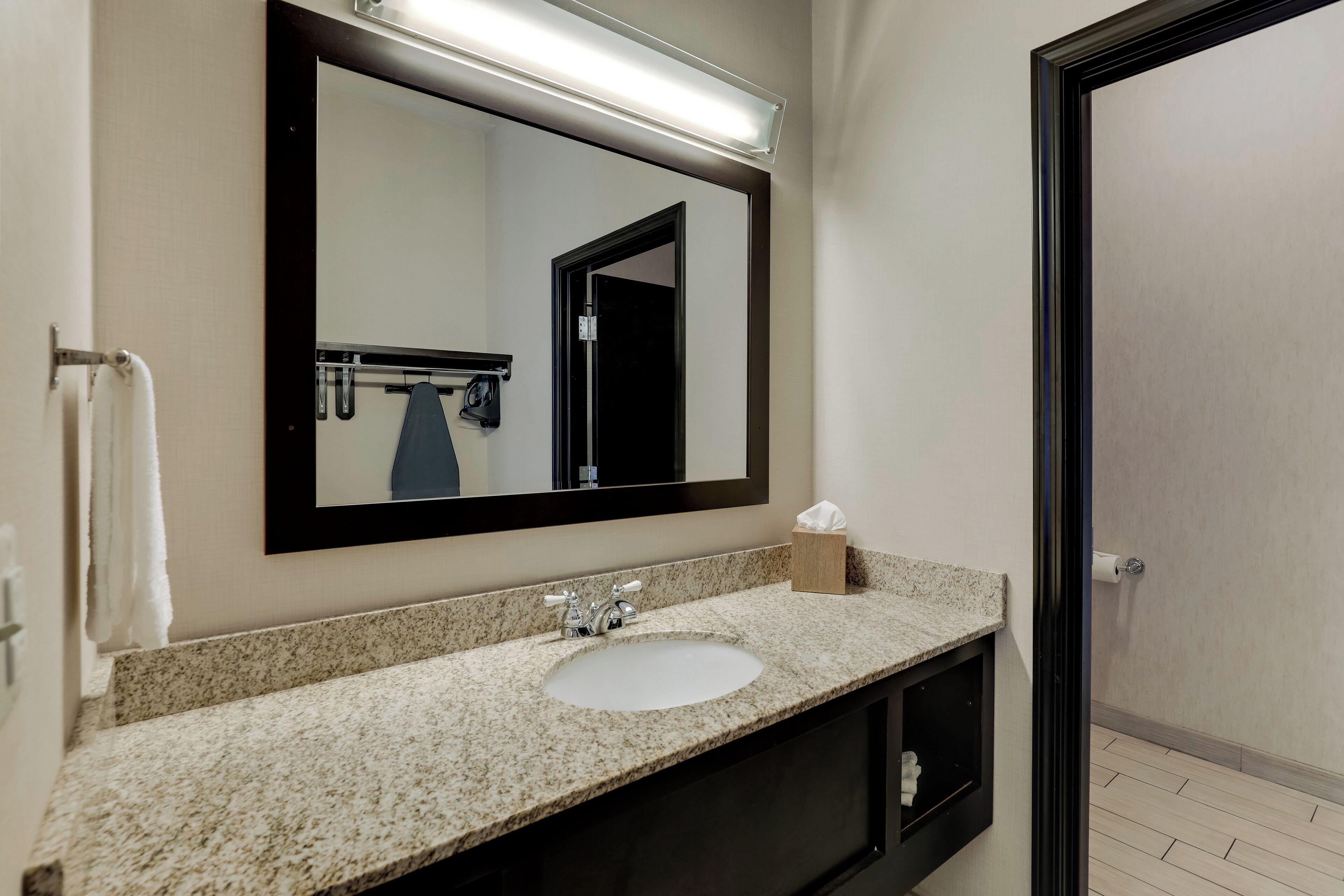 A bathroom with a granite countertop sink, a mirror, a towel rack, and a door.