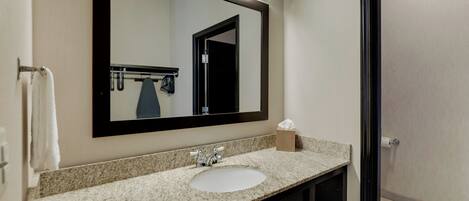 A bathroom with a granite countertop sink, a mirror, a towel rack, and a door.