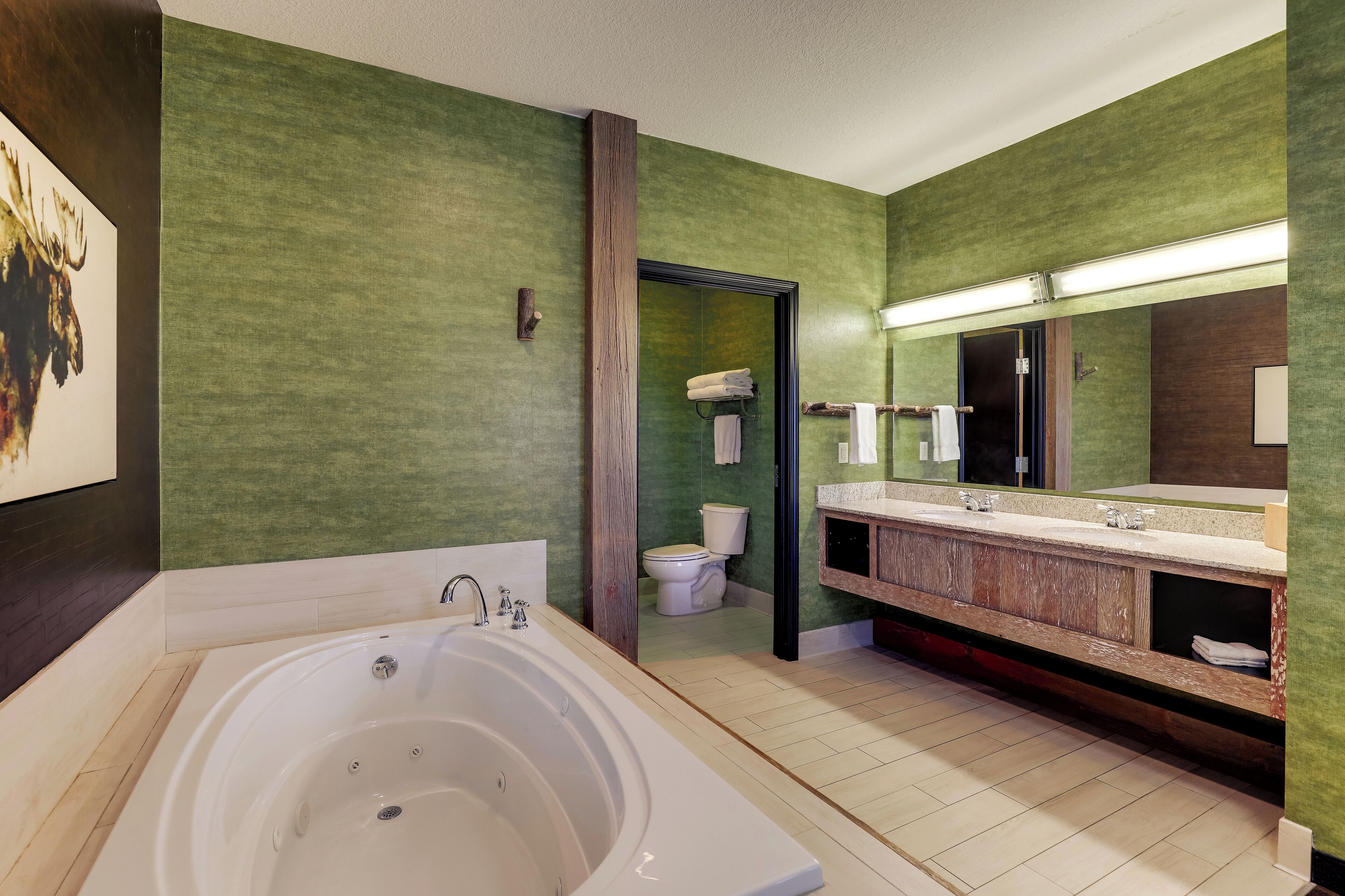 A modern bathroom with a large bathtub, a vanity with a mirror, and a toilet visible through an open door.