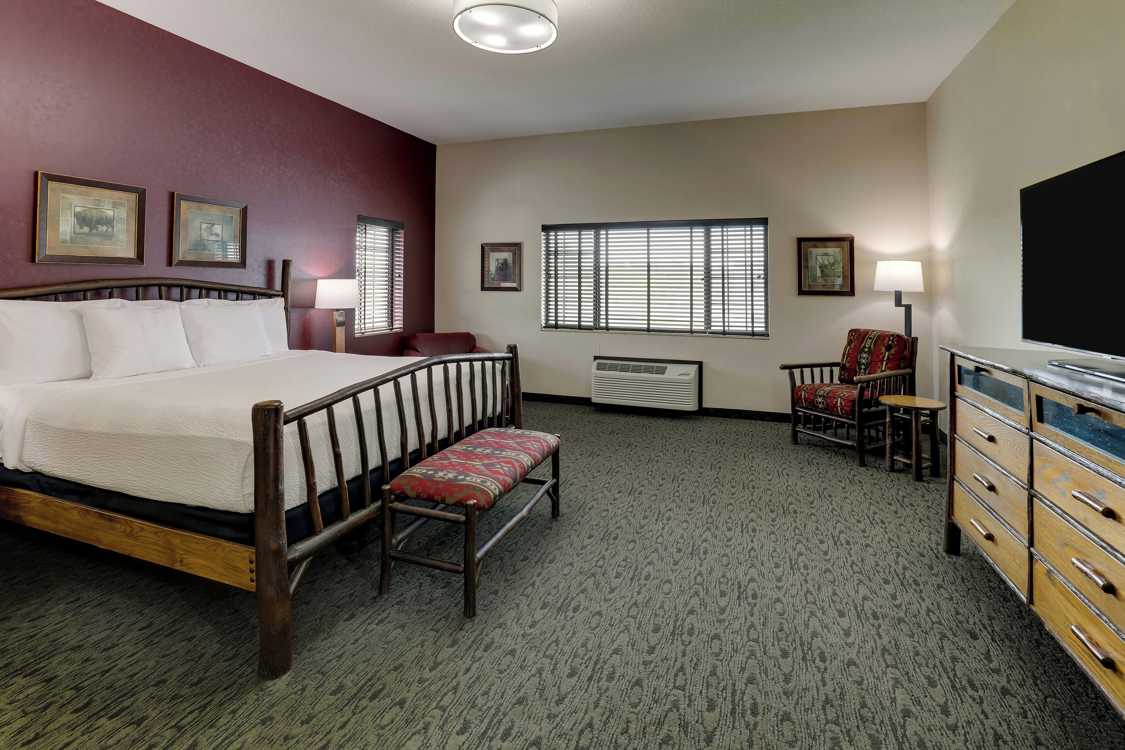 A hotel room with a bed, a bench, a dresser, a chair, a table, and a window with blinds.