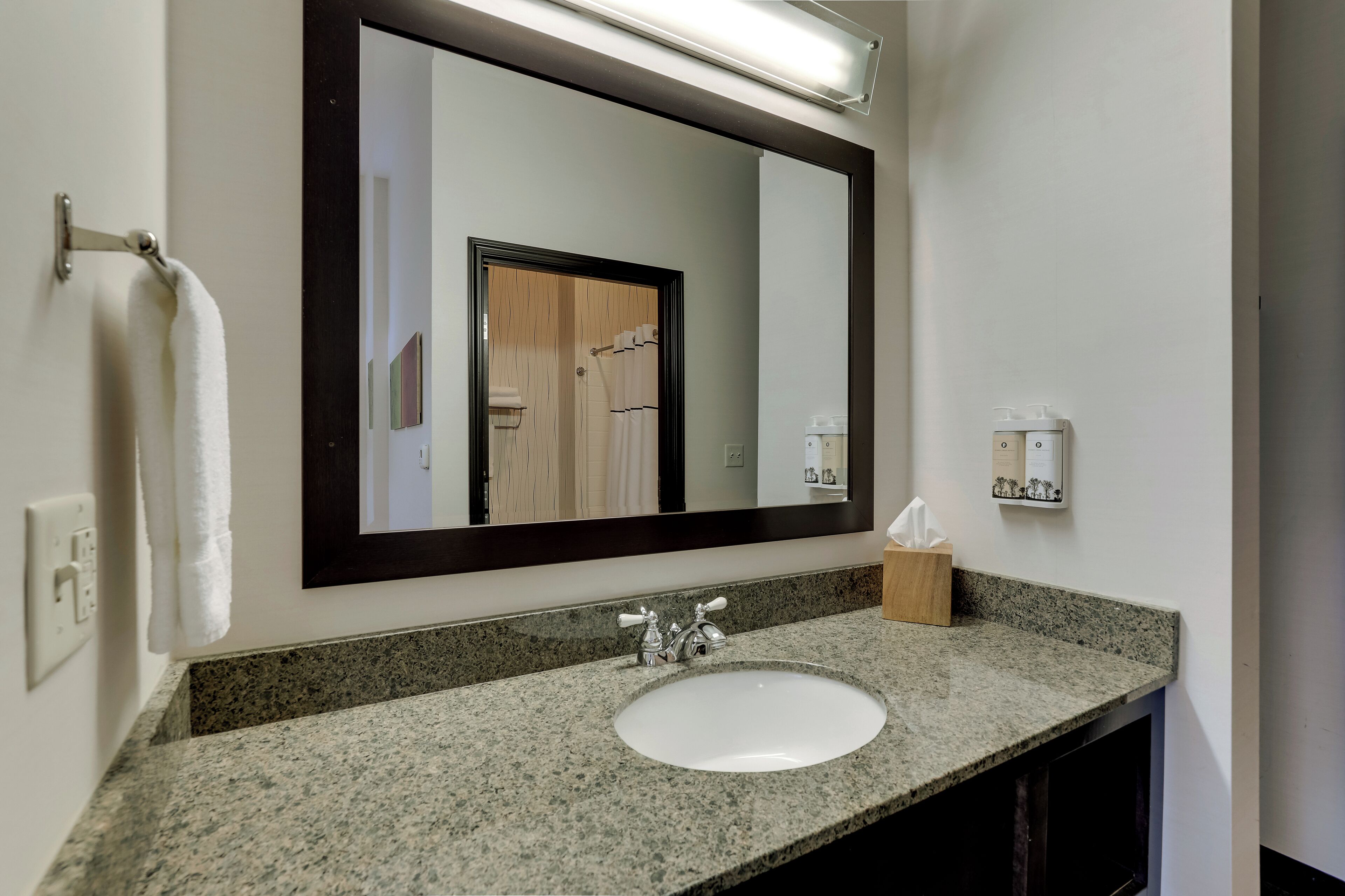A bathroom with a granite countertop, a white sink, a large mirror, and a towel rack.