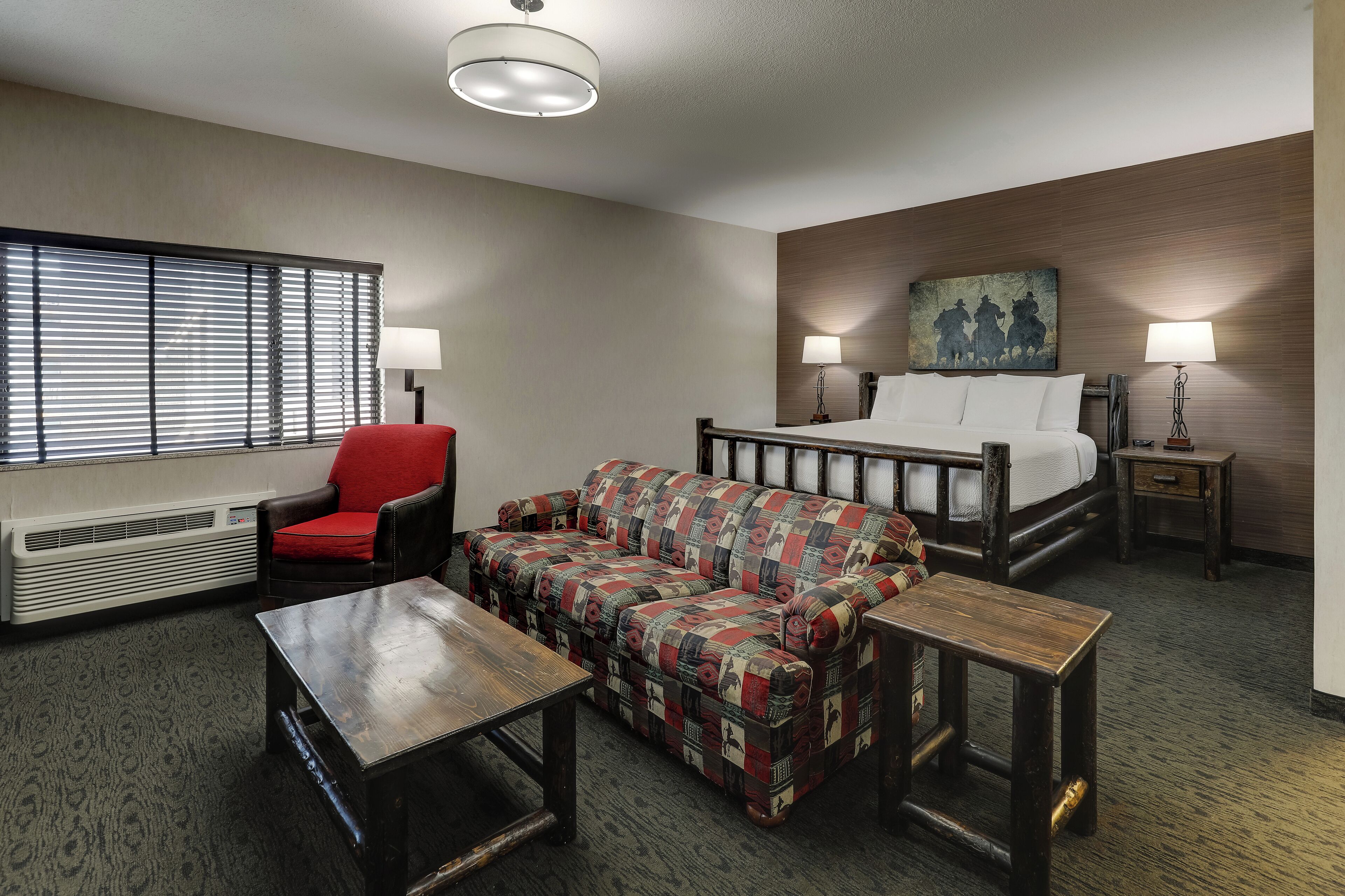 A hotel room with a bed, a sofa, a chair, a table, and a heater.
