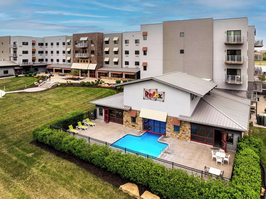 A modern hotel with a swimming pool, outdoor seating, and a well-maintained lawn.