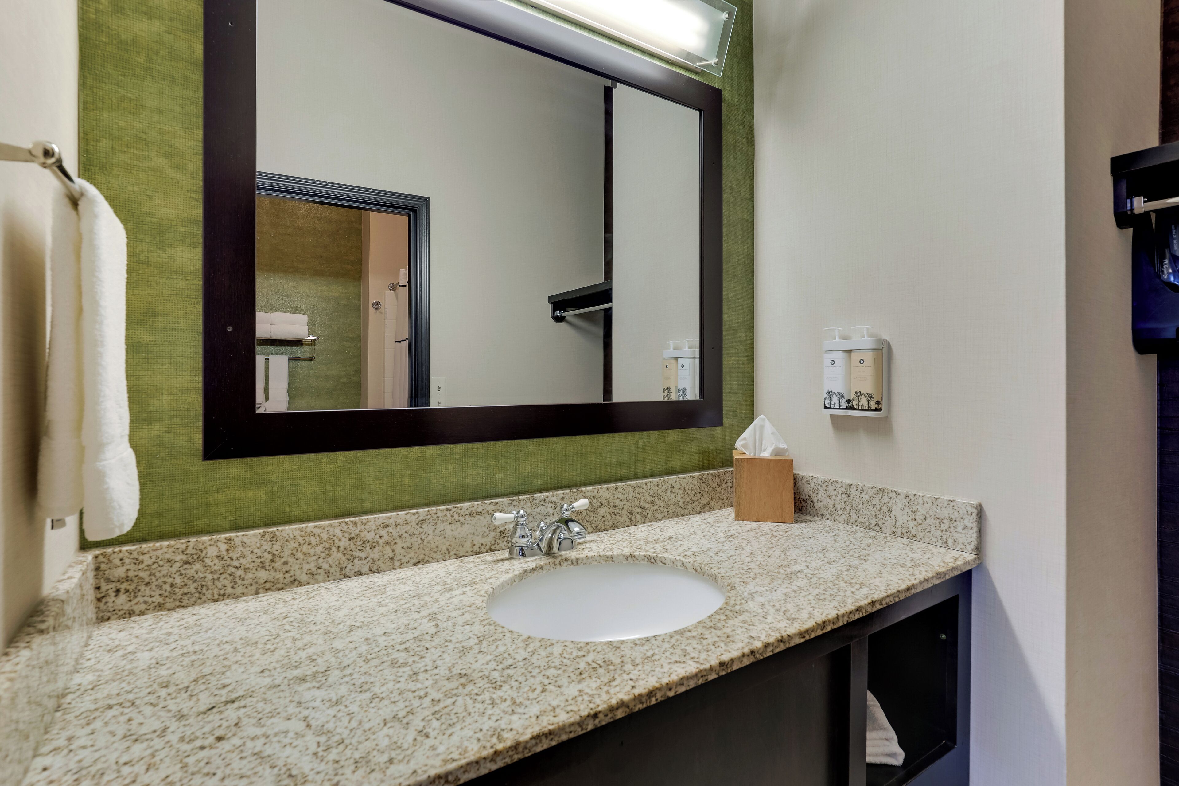 A bathroom with a large mirror, a sink, and a towel rack.