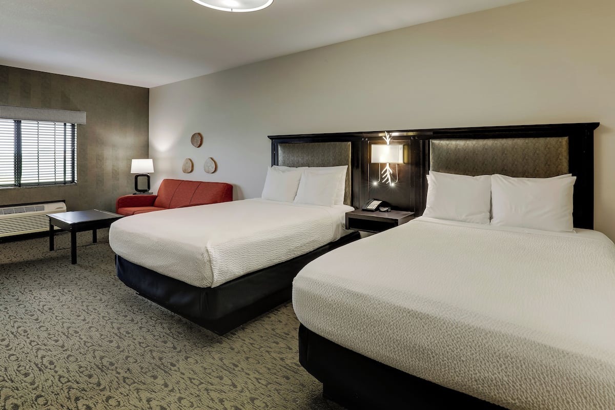 Une chambre d’hôtel avec deux lits, une chaise rouge, une petite table, une lampe et un téléphone fixé au mur.