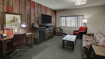 A furnished living room with a wooden accent wall, a flat-screen TV, a desk with a chair, a sofa, and a window with blinds.