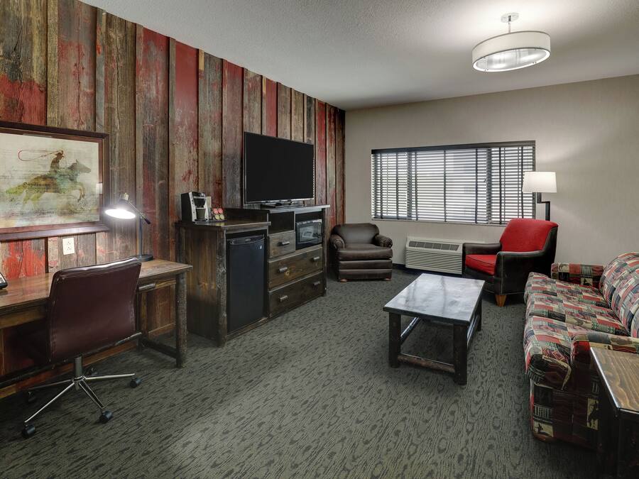 A furnished living room with a wooden accent wall, a flat-screen TV, a desk with a chair, a sofa, and a window with blinds.