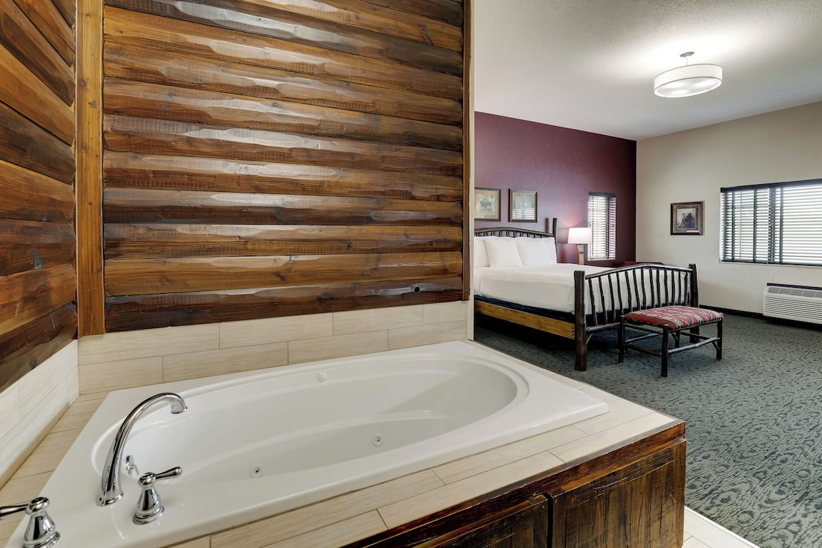 Une salle de bain avec une grande baignoire, un lambris en bois, un lit avec une tête de lit et une chaise.