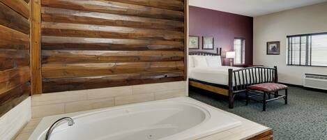 A bathroom with a large bathtub, wooden wall paneling, a bed with a headboard, and a chair.