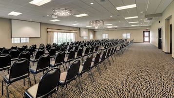 A conference room with rows of chairs, a projector screen, and a carpeted floor.