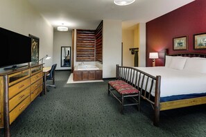 A hotel room with a large bed, a desk with a television, a bathroom with a bathtub, and a wooden wall panel.