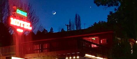Ein Motel mit leuchtendem Neonzeichen, einer überdachten Außenbestuhlung und einem sichtbaren Halbmond am Himmel.