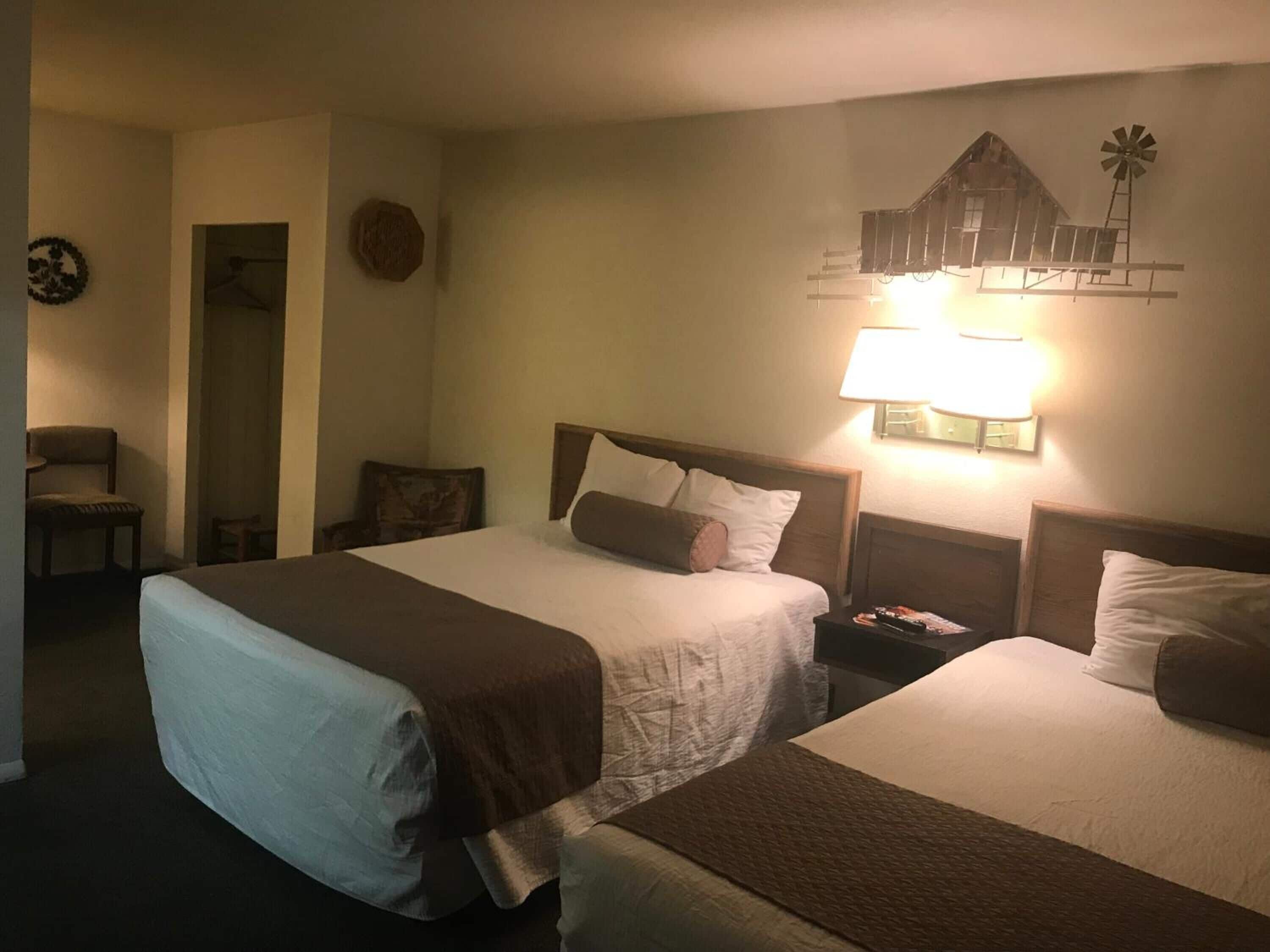 Une chambre d’hôtel avec deux lits, une table de chevet avec une lampe, une chaise et un décor mural représentant un moulin à vent.