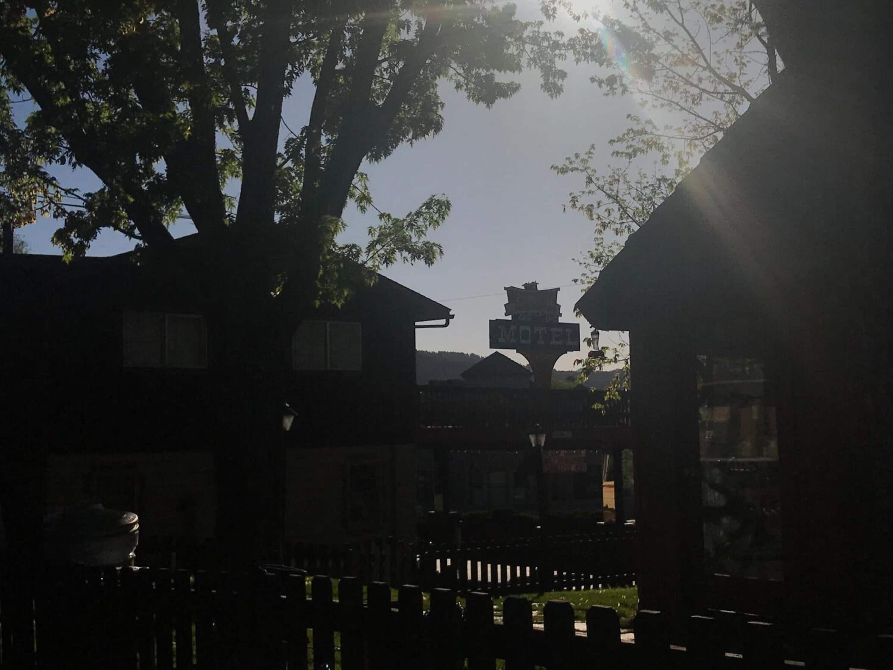 A motel with a signboard, surrounded by trees and a fence.