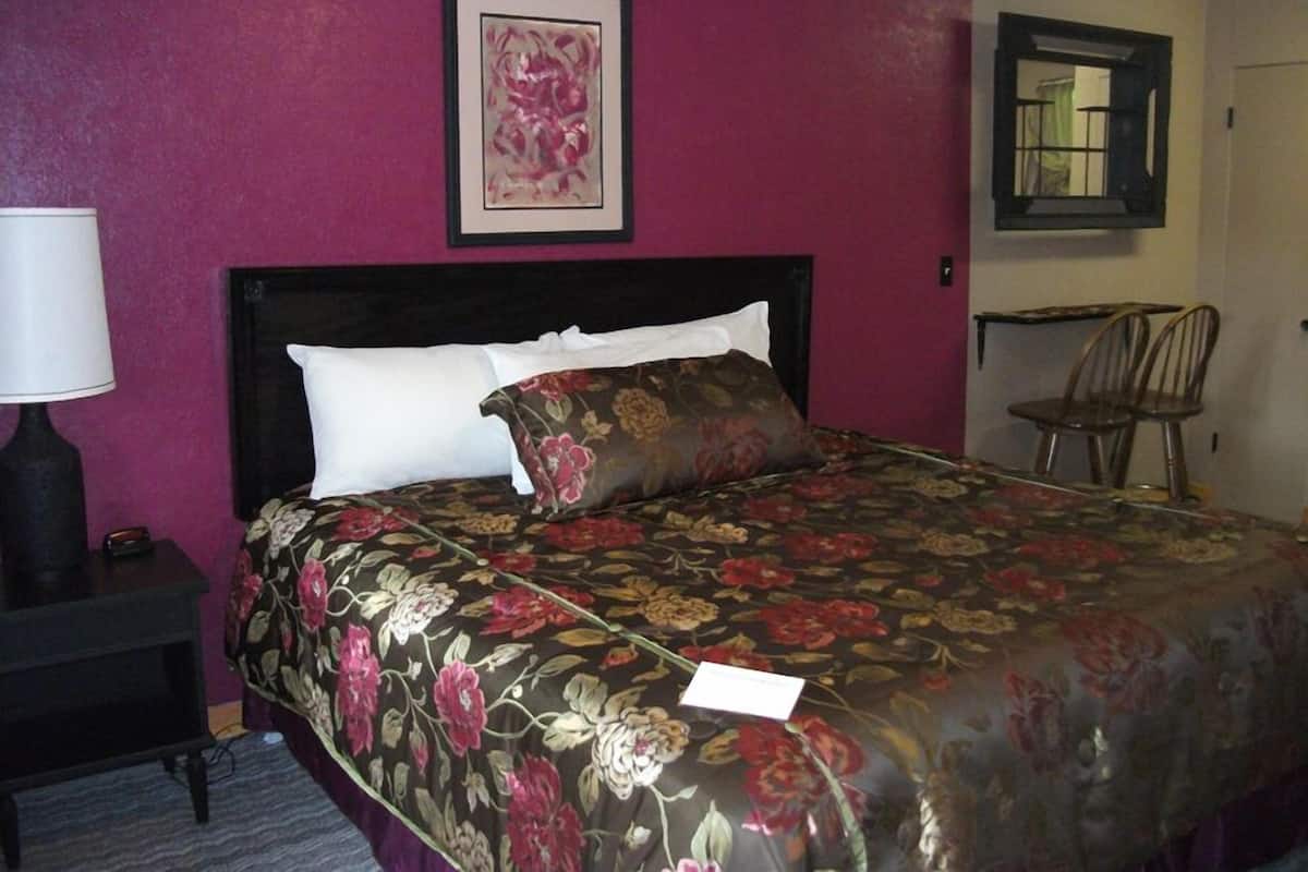A hotel room with a bed, a nightstand, a chair, and a framed artwork on the wall.