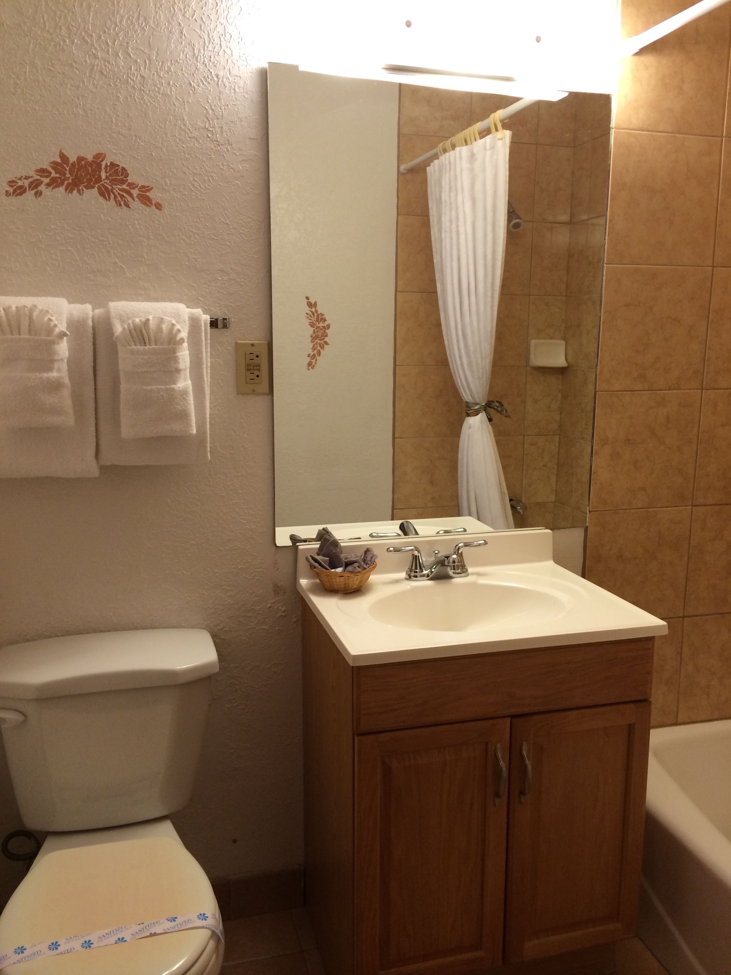 Une salle de bain avec des toilettes, un lavabo et une baignoire. Des serviettes sont accrochées au mur et un miroir se trouve au-dessus du lavabo.