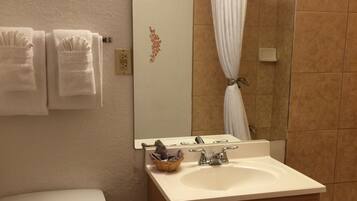 Une salle de bain avec des toilettes, un lavabo et une baignoire. Des serviettes sont accrochées au mur et un miroir se trouve au-dessus du lavabo.