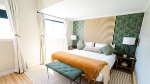 Quarto com cama, banco, mesas de cabeceira, luminárias e vista para o exterior.