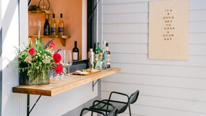 Uma área de bar com uma prateleira de madeira exibindo garrafas, copos e um arranjo floral.