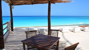 A wooden deck with a table and chairs, overlooking a beach with clear blue water. - Amigo Rental (Cancun)
