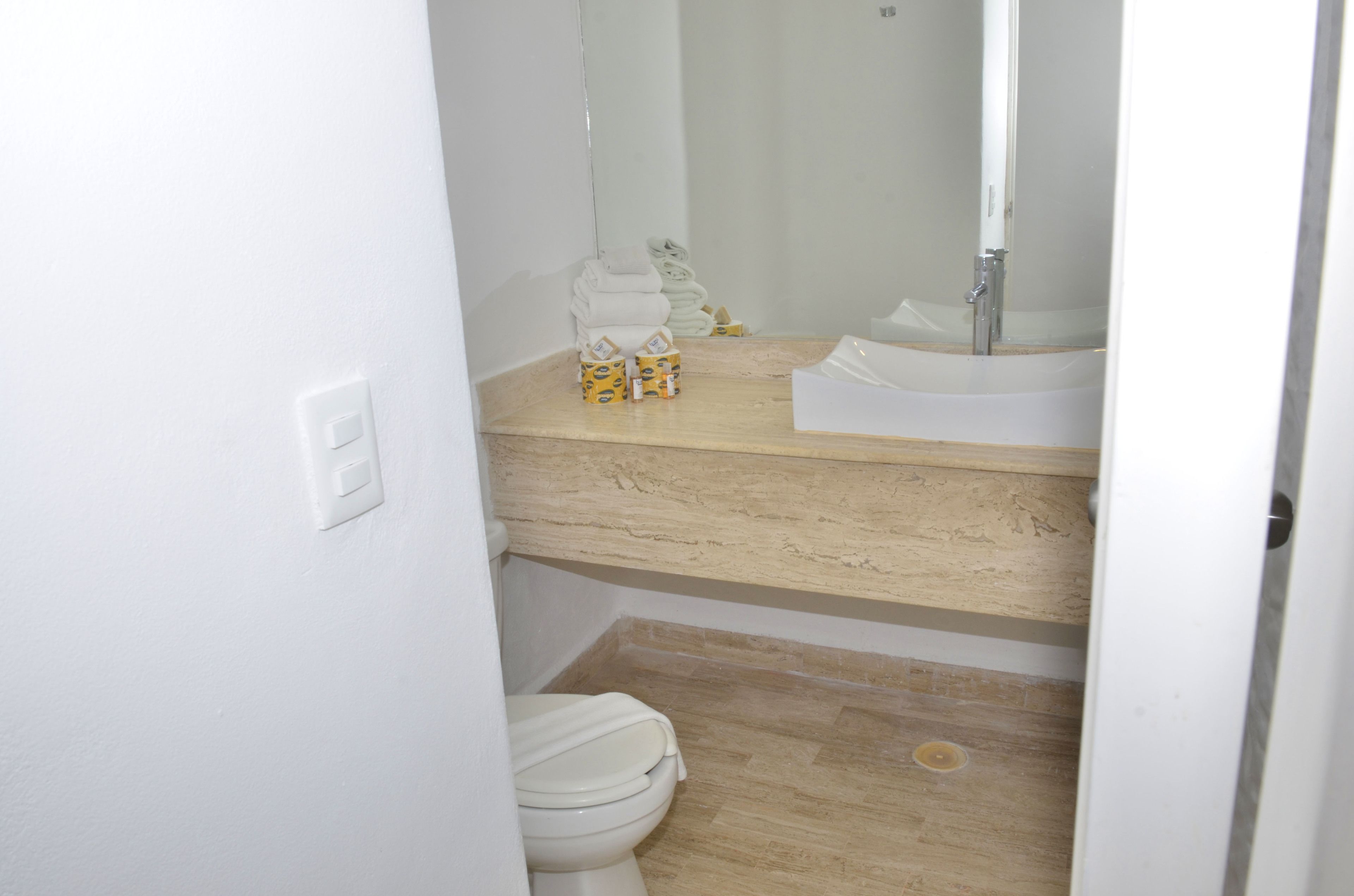 A bathroom with a toilet, sink, and mirror. There are towels and toiletries on the counter.