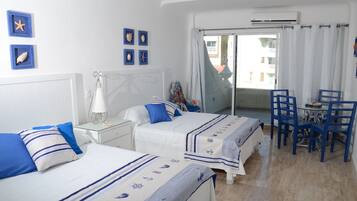 A hotel room with two beds, a dining table with chairs, and a view of the outside.