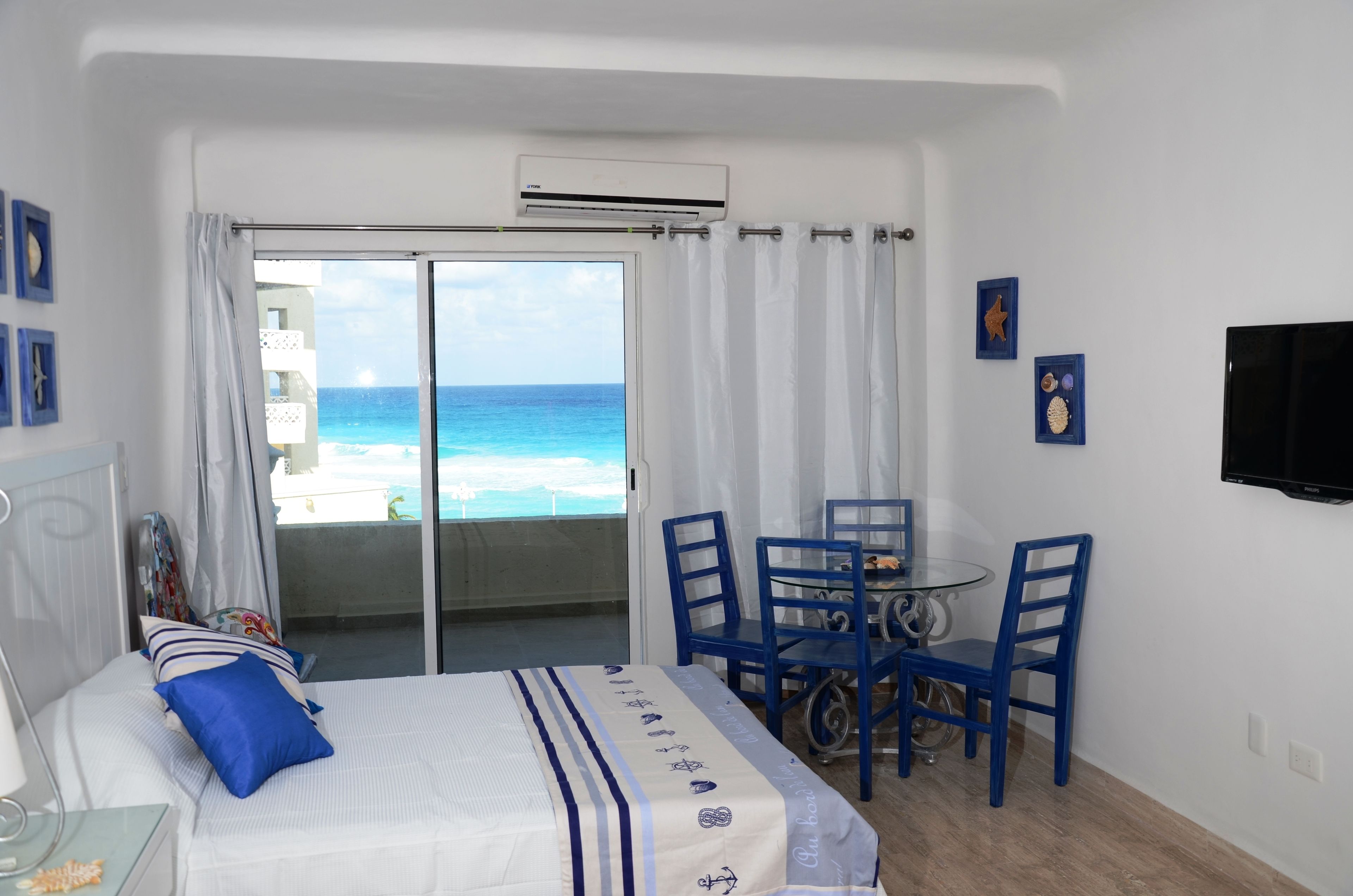 Un dormitorio con cama, una mesa con sillas, televisión y vista al océano.