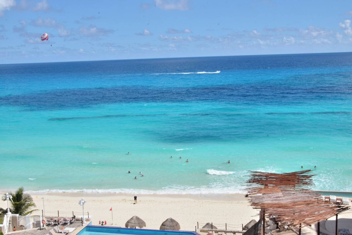 A beach with clear turquoise waters, a sandy shore, and a few umbrellas.