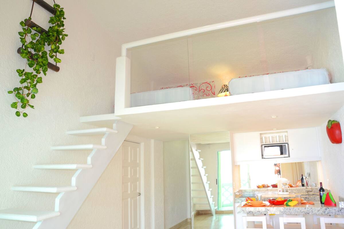 A modern kitchen with a central island, white cabinetry, and a staircase leading to an upper level.