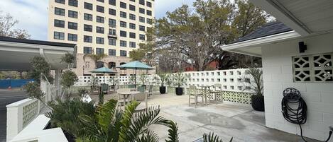 A hotel patio with outdoor seating, a white fence, and a tall building in the background.