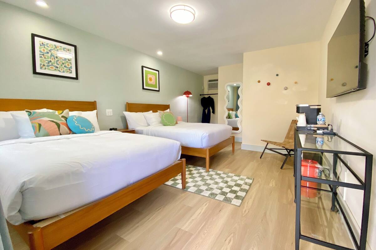 A hotel room with two beds, a desk, a chair, a mirror, and a flat-screen TV.