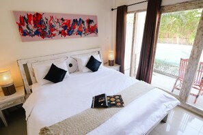 Una cama bien hecha con sábanas blancas y dos almohadas negras, una mesita de noche con una lámpara, y un cuadro abstracto grande sobre la cama.
