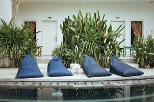 A poolside area with blue cushions, a small white table, and lush green plants.
