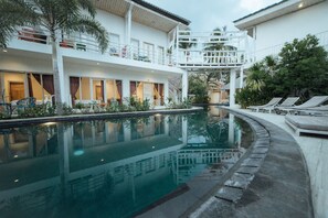 Zona de piscina con sillones de descanso, una palmera y un edificio con varios balcones.