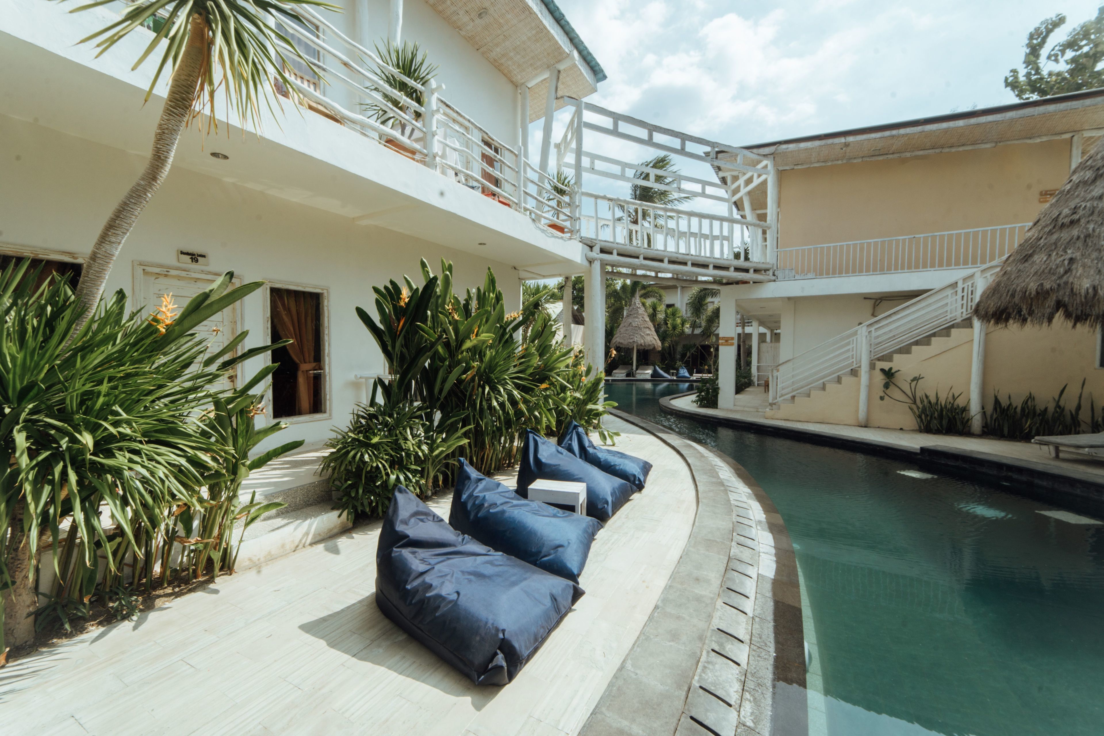 Área da piscina com espreguiçadeiras, escada e estrutura de telhado de palha.