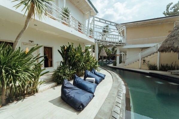 Área da piscina com espreguiçadeiras, escada e estrutura de telhado de palha.