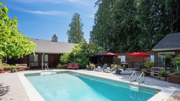 A rectangular swimming pool with a tiled edge, surrounded by lounge chairs and a barbecue area. - Sunshine Lodge (Gibsons)